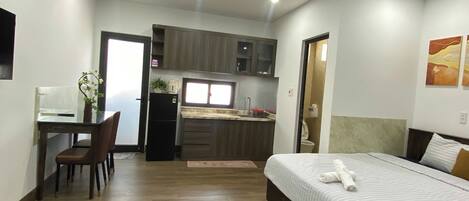 A compact hotel room with a bed, a desk, a chair, a small kitchenette, and a bathroom.
