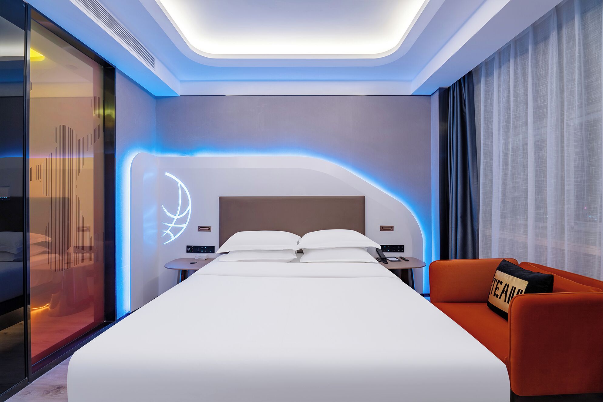Una habitación de hotel moderna con una cama grande, un escritorio con una silla, un sofá y una pared con un diseño de iluminación original.