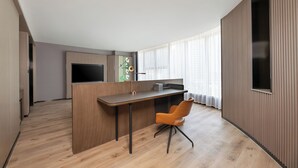 A modern hotel room with a wooden desk, a flat-screen TV, and a large window with curtains.
