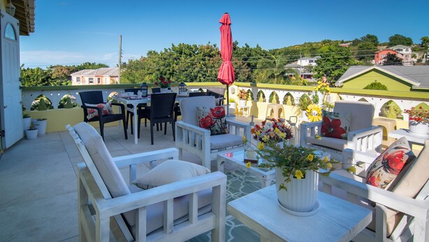 Eine Terrasse mit weißer Möbel, einem roten Sonnenschirm und einer Blumenvase.