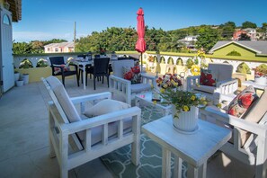 A patio with white furniture, a red umbrella, and a flower vase. - Exquisite 3-bedroom house in tranquil Mount Pleasant. (St Johns)