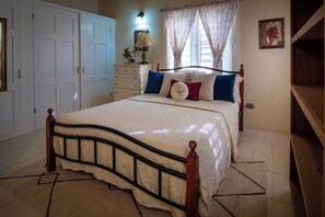 A bedroom with a four-poster bed, a dresser, a lamp, and a window with curtains. - Exquisite 3-bedroom house in tranquil Mount Pleasant. (St Johns)