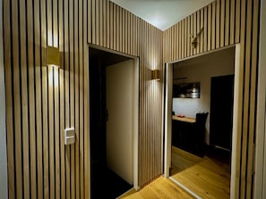 Ein Zimmer mit Holzbodenpaneelen, einer Tür, einem Lichtschalter und einem kleinen Tisch mit einem Stuhl.
