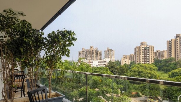 A balcony with chairs and a table, overlooking a cityscape with high-rise buildings and greenery.
