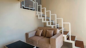 A modern living room with a beige sofa, a black ottoman, and a white staircase with geometric design. - AF Nexura Escapes (Garung)