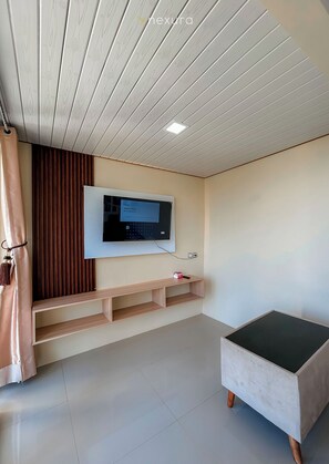 Una habitación moderna con una televisión de pantalla plana montada en la pared, un estante de madera, un banco acolchado y un techo con paneles de madera.