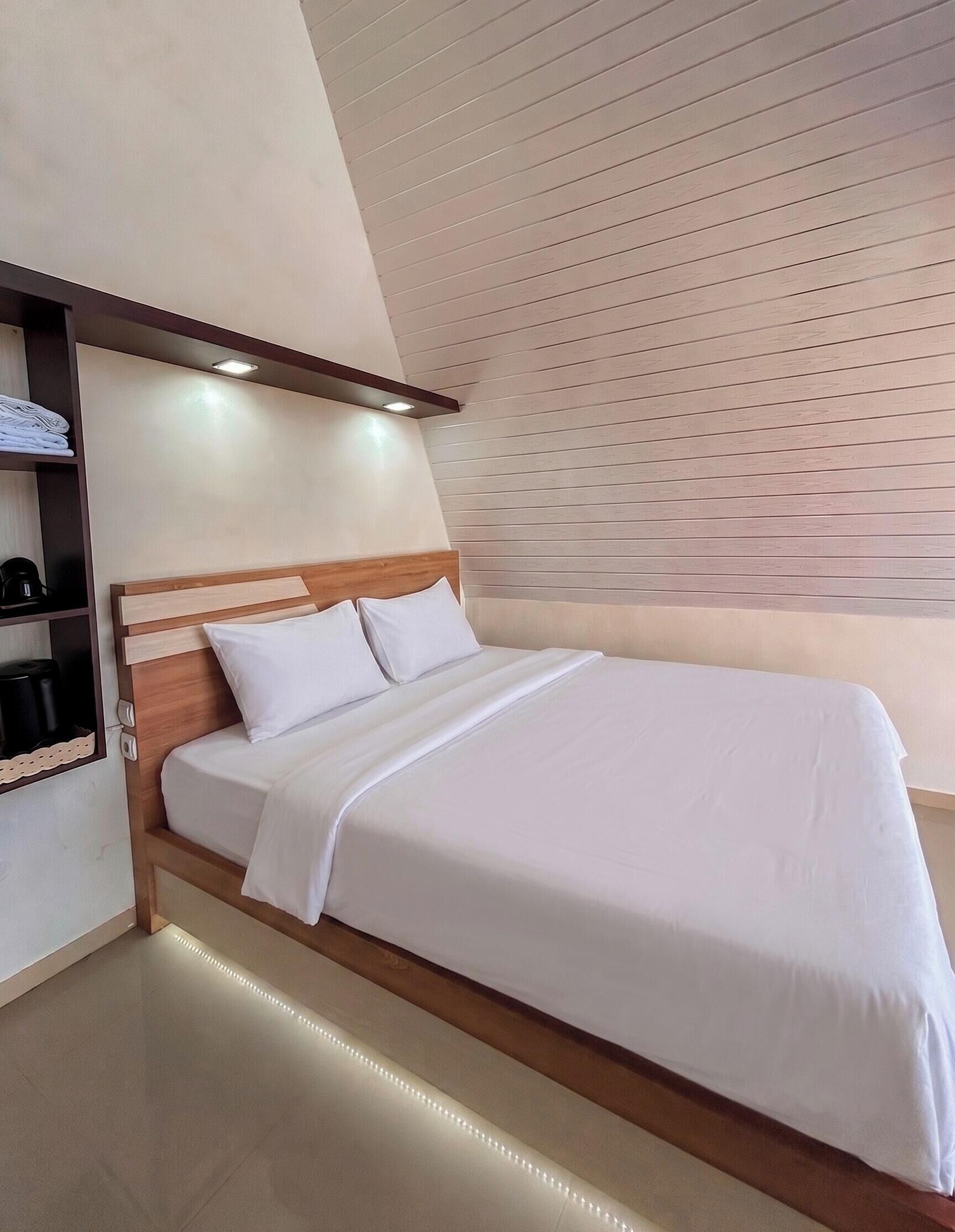 Une chambre d’hôtel moderne avec une tête de lit en bois, un lit parfaitement fait et une étagère intégrée avec une machine à café.