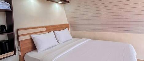 Une chambre d’hôtel moderne avec une tête de lit en bois, un lit parfaitement fait et une étagère intégrée avec une machine à café.