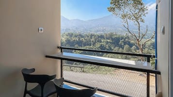 A balcony with a view of a mountainous landscape, a table with two chairs, and a gas cylinder.