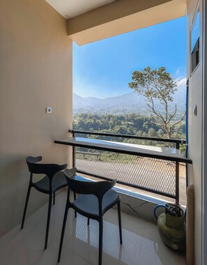 Un balcón con vistas a un paisaje montañoso, una mesa con dos sillas y un cilindro de gas.