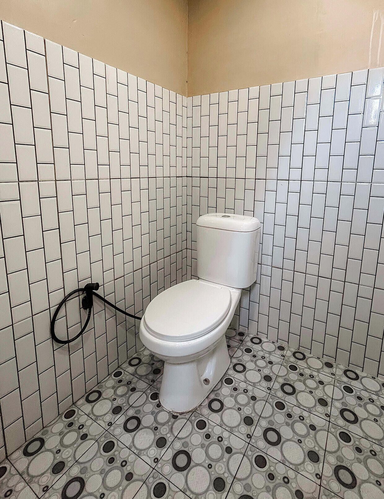 A bathroom with white tiled walls and floor, a toilet, and a toilet paper holder.