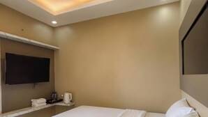 Habitación de hotel con una cama grande, un televisor de pantalla plana montado en la pared y una cafetera sobre una mesita.