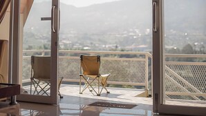 Una habitación con un amplio ventanal corredera que da a un balcón con vistas a una cadena montañosa.