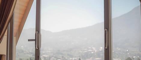 Una habitación con un amplio ventanal corredera que da a un balcón con vistas a una cadena montañosa.