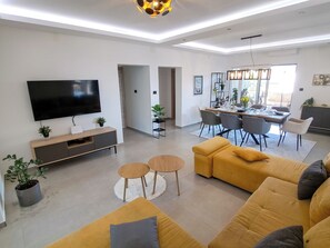 A modern living room with a flat-screen TV, a sofa set, a dining area with a table and chairs, and a kitchen area. - Apartment Nona by Interhome (Medulin)