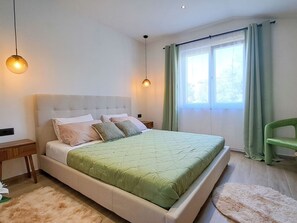 A bedroom with a bed, bedside tables, a nightstand, a chair, a window with curtains, and hanging lamps. - Apartment Nona by Interhome (Medulin)