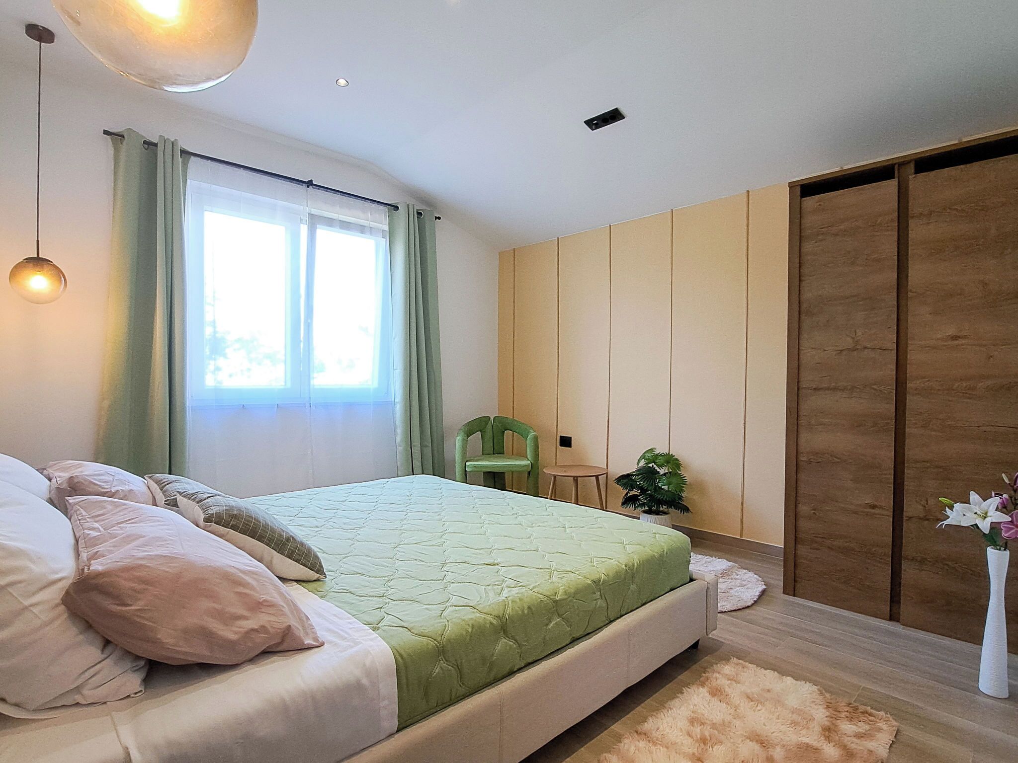 A bedroom with a bed, a chair, a small table, a potted plant, and a sliding door.