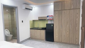 A compact kitchen with a sink, a black refrigerator, wooden cabinets, and an air conditioning unit. - Na Uy Apartment (Bac Nha Trang)