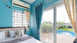 A bedroom with a bed, a window with curtains, an air conditioning unit, and a view of a swimming pool.