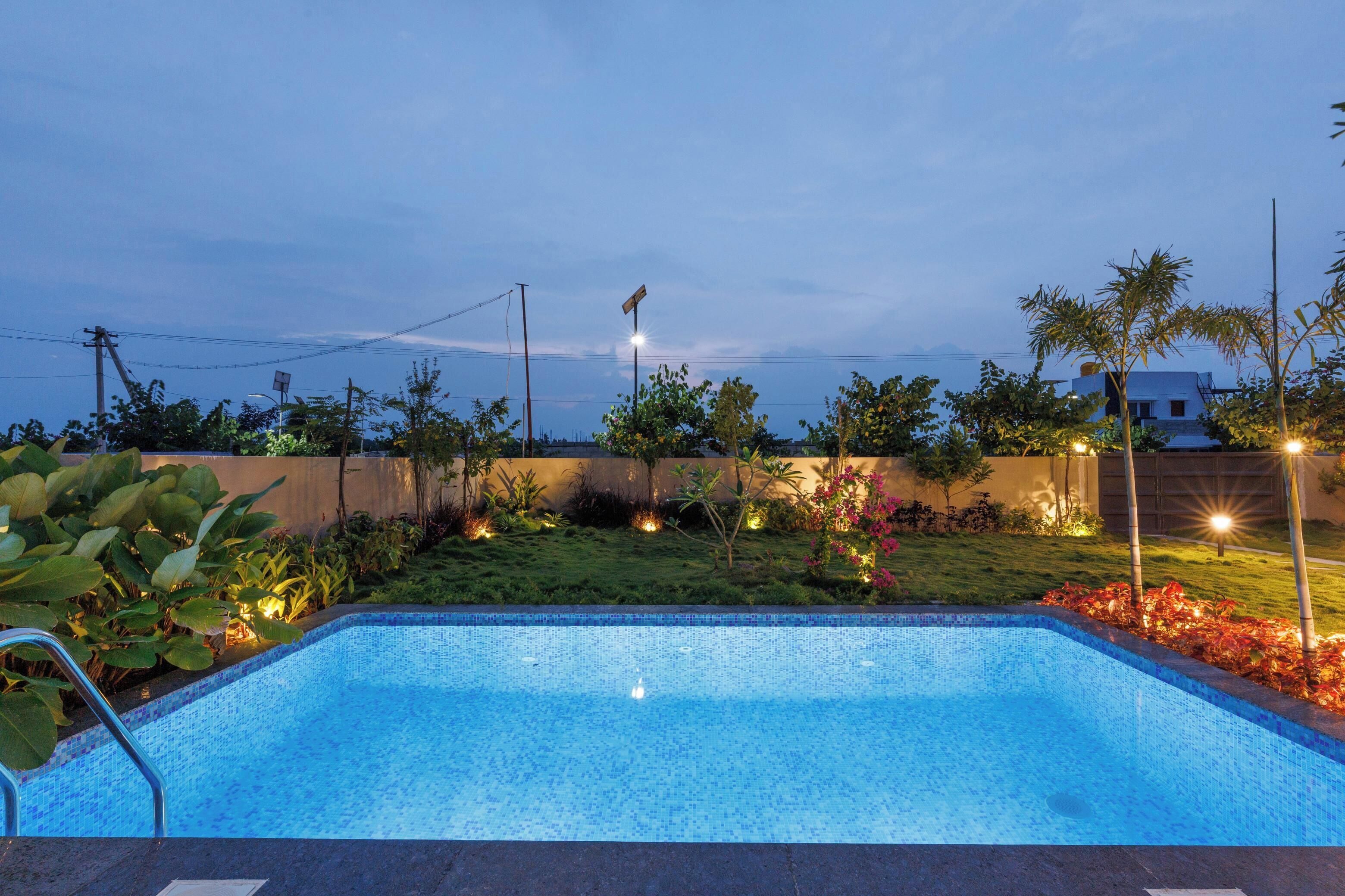 A swimming pool with a tiled edge, surrounded by a landscaped garden with various plants and a fence.