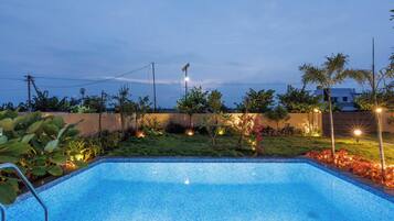 A swimming pool with a tiled edge, surrounded by a landscaped garden with various plants and a fence.