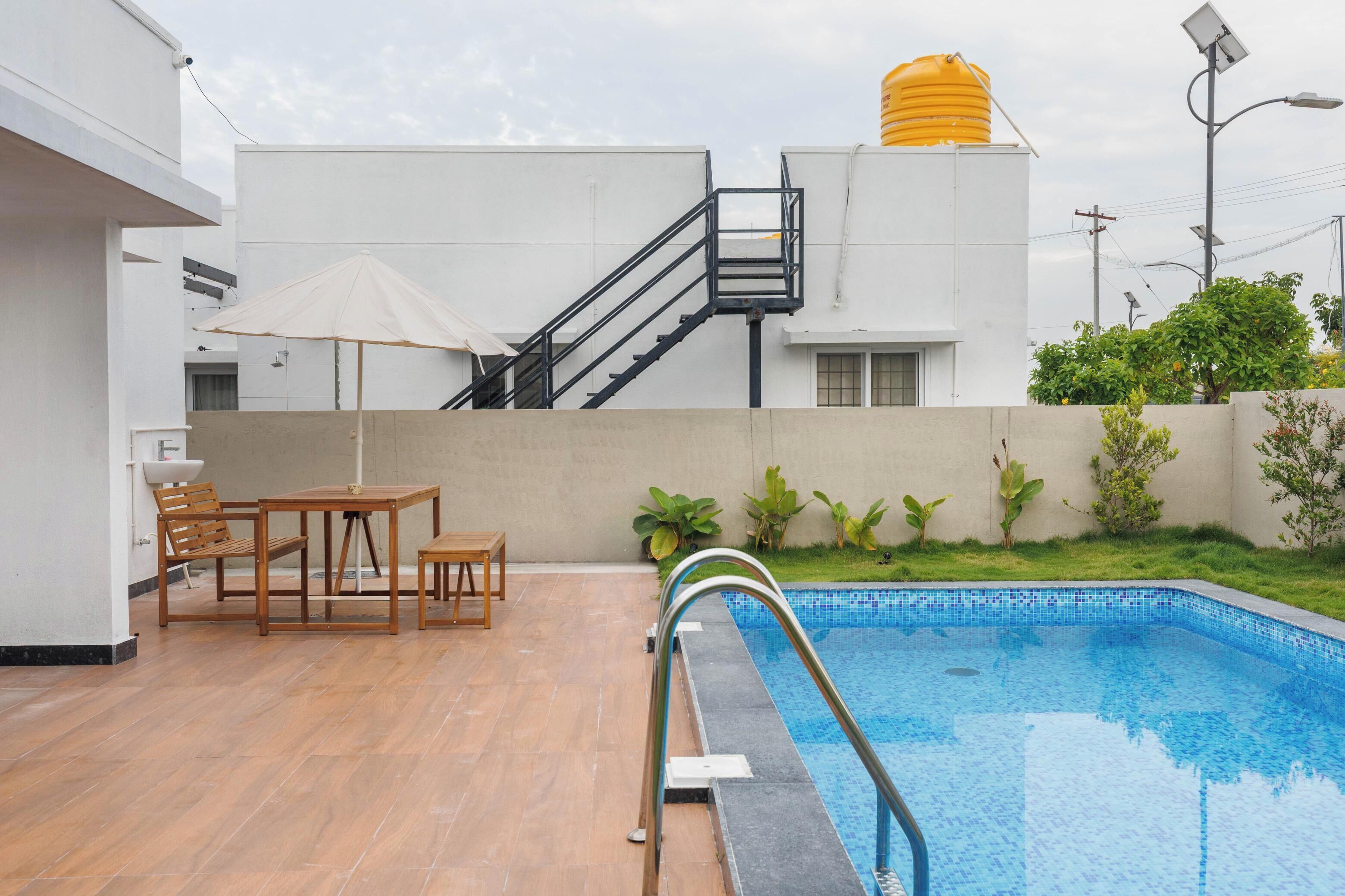 A swimming pool with a metal ladder, wooden furniture, and a yellow water tank in the background.