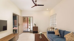 A modern living room with a sofa, coffee table, TV, and a ceiling fan. - Stonehill Villa Nr Airport 30min Nandi Hills (Bengaluru)