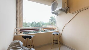 Una habitación con ventana, dos taburetes, una cama y un equipo de aire acondicionado.