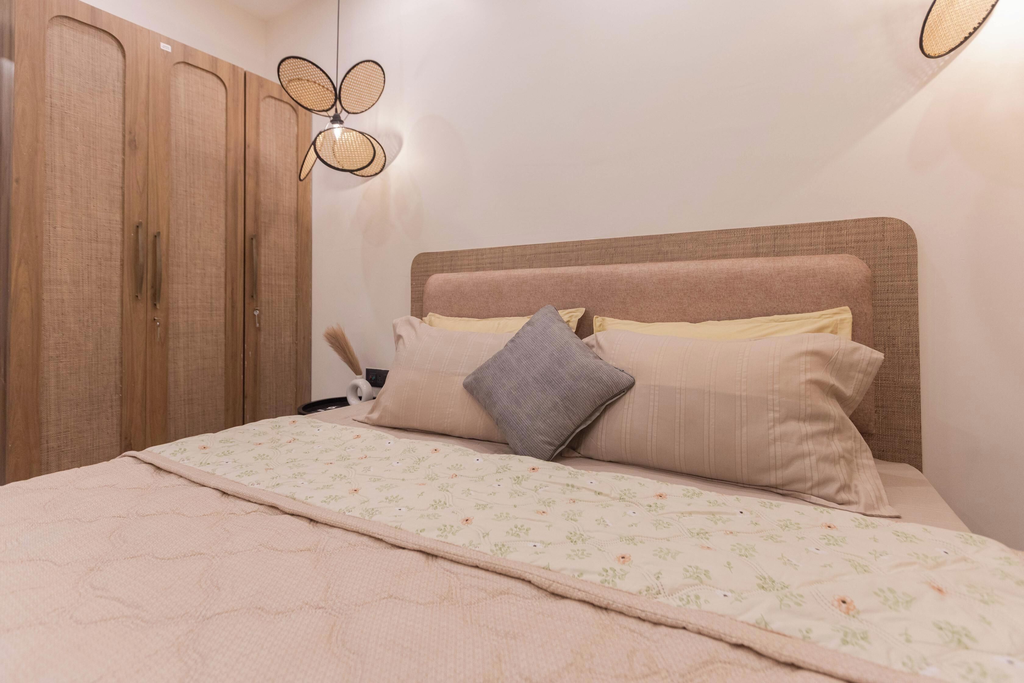 A bedroom with a bed, pillows, a headboard, a wardrobe, and a wall-mounted light fixture.