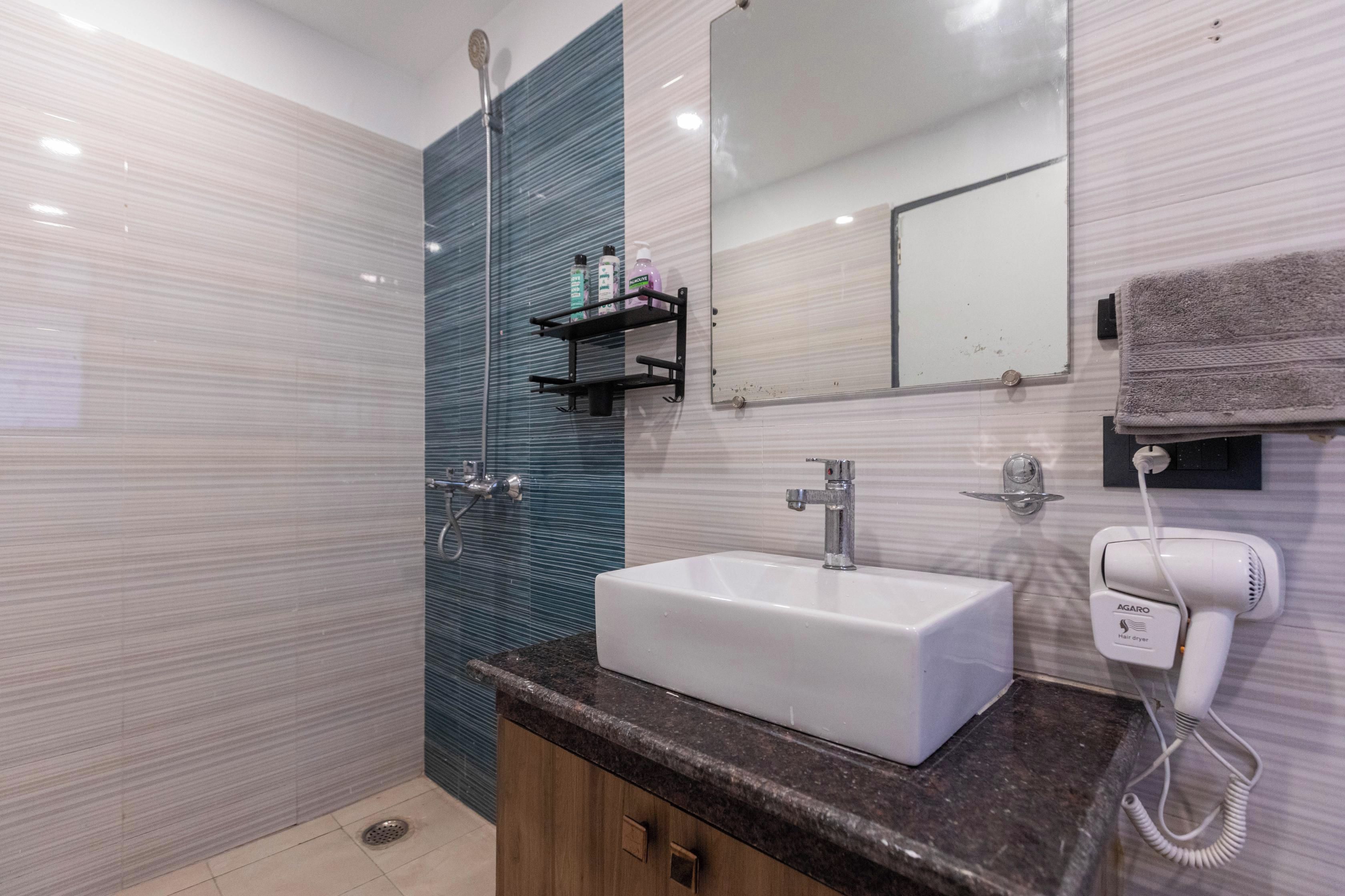 Een moderne badkamer met een wit wastafelmeubel, een spiegel, een haardroger en een douche.