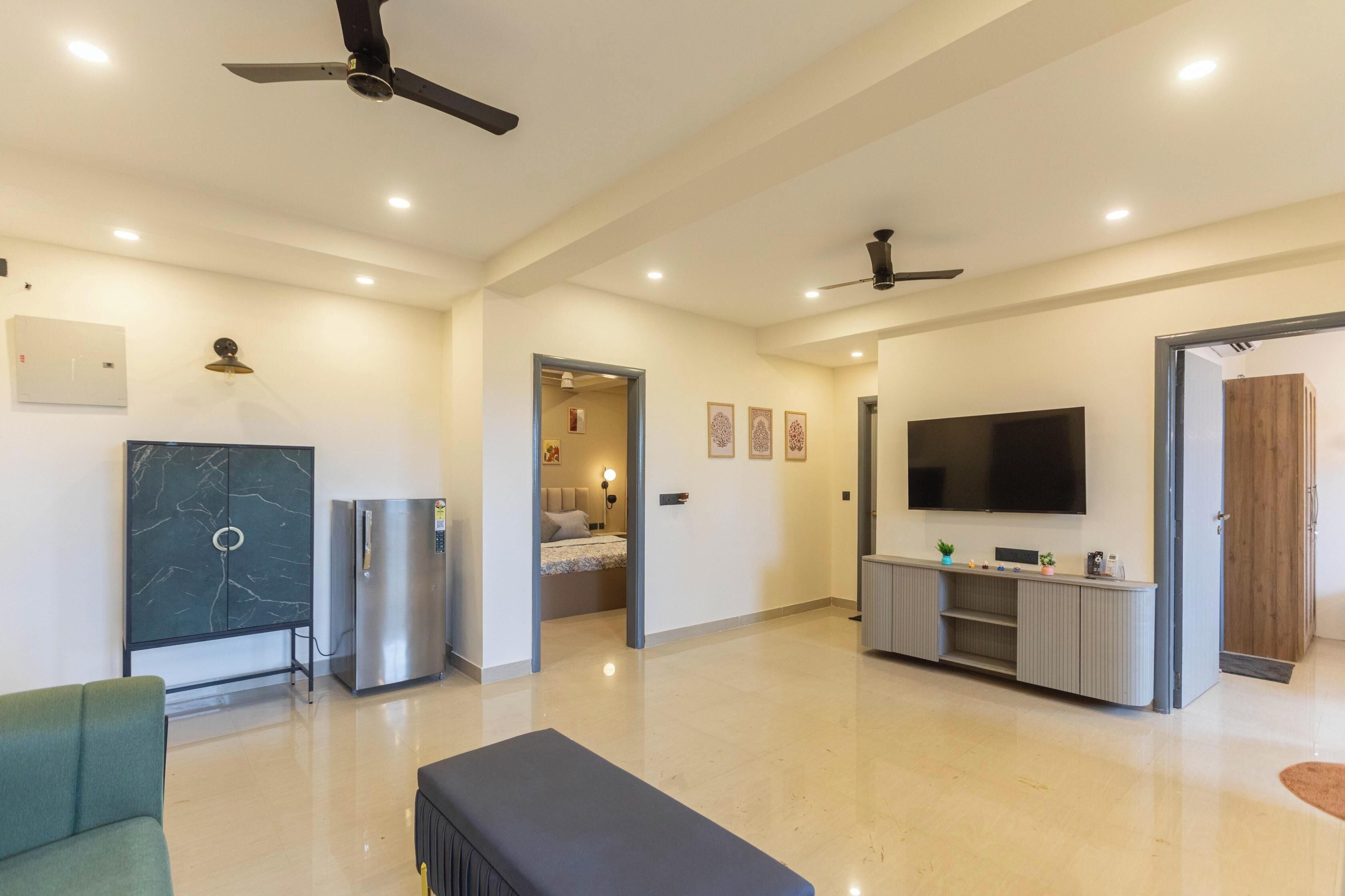 Amplia sala de estar con una televisión de pantalla plana grande, ventiladores de techo, un mueble de mármol, un refrigerador y un sofá.