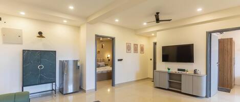 Amplia sala de estar con una televisión de pantalla plana grande, ventiladores de techo, un mueble de mármol, un refrigerador y un sofá.