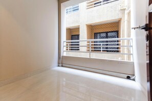 A room with a tiled floor, a white railing, and a view of a building with multiple windows and balconies. - Vedastay by Jadecaps 2bhk Vedic Village Kolkata (Barasat)