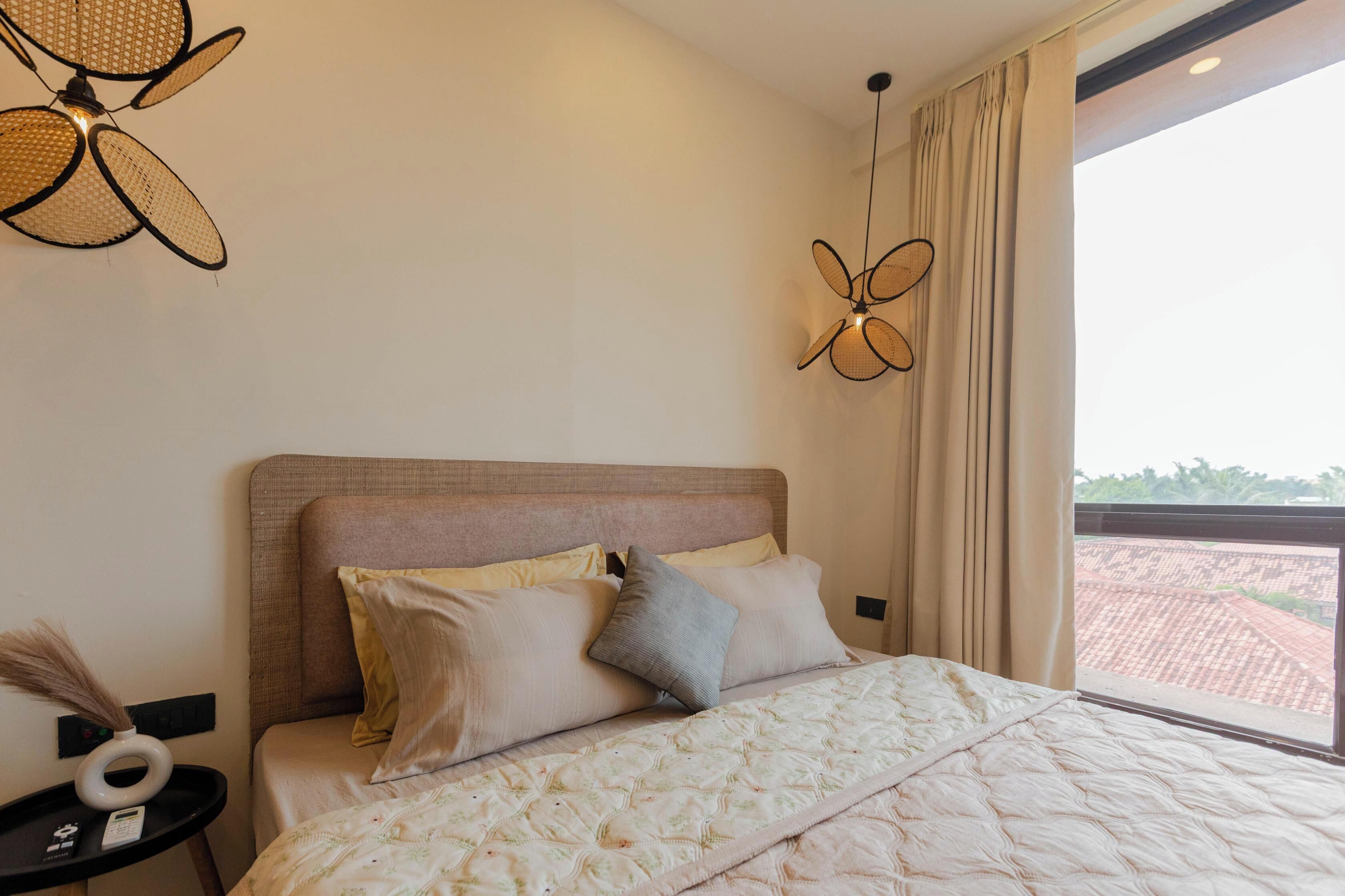 Un dormitorio con cama, almohadas, una mesita de noche con un florero y un ventilador de techo.