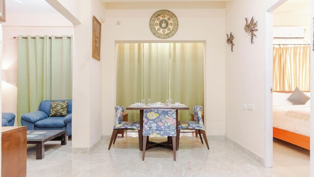 A room with a dining table, chairs, a sofa, and a bed. - Elara Residences by Jadecaps2bhknr IIM Kolkata (Alipur)