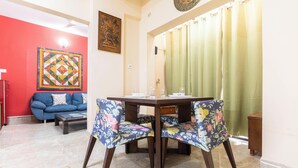 A dining area with a table and chairs, a sofa, a patterned wall, and a curtain. - Elara Residences by Jadecaps2bhknr IIM Kolkata (Alipur)