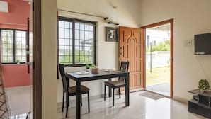 A dining area with a table and chairs, a window with a view, a door leading outside, and a wall-mounted television. - Jhilmil Escape Pool Garden 1hr Koramangala HSR (Hosur)