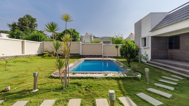 A modern residential setting with a swimming pool, a well-maintained lawn, and a house with a contemporary design. - Jhilmil Escape Pool Garden 1hr Koramangala HSR (Hosur)