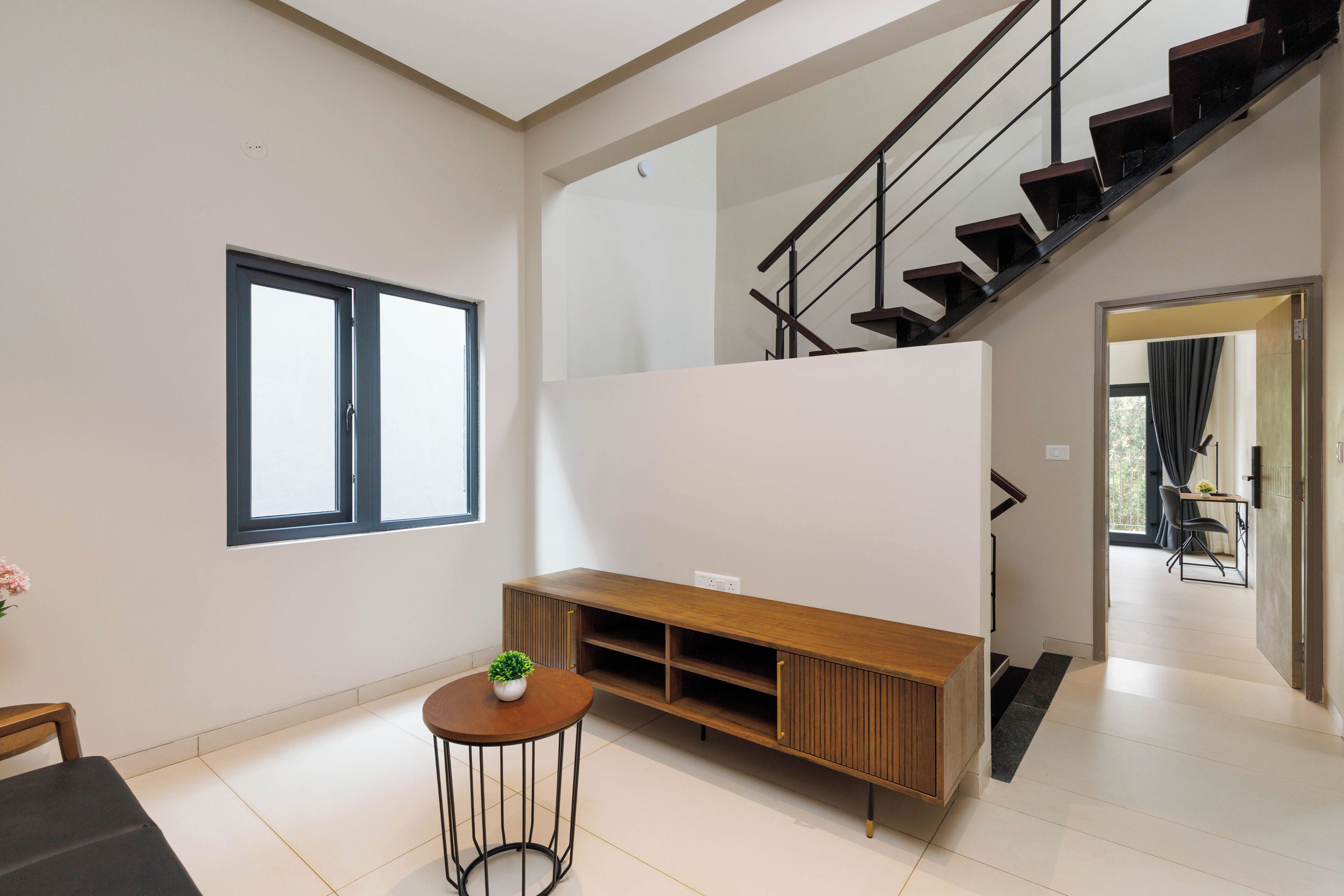 A modern living room with a wooden entertainment unit, a staircase, and a view of a dining area.