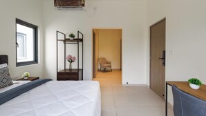 Une chambre à coucher comprenant un lit, une table de chevet, un miroir, une chaise et une porte donnant sur une autre pièce.