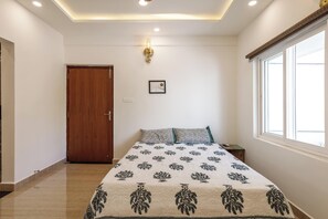 A bedroom with a bed, a nightstand, a wall-mounted light fixture, a door, and a window.
