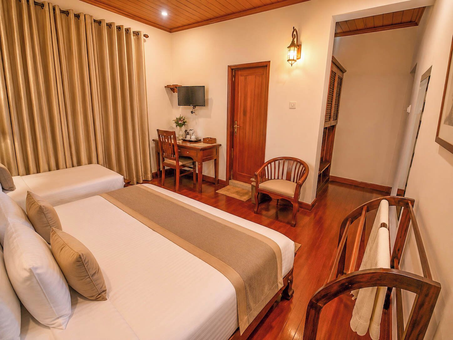 Une chambre d’hôtel avec deux lits, un bureau avec une chaise, une télévision et un escalier en bois.
