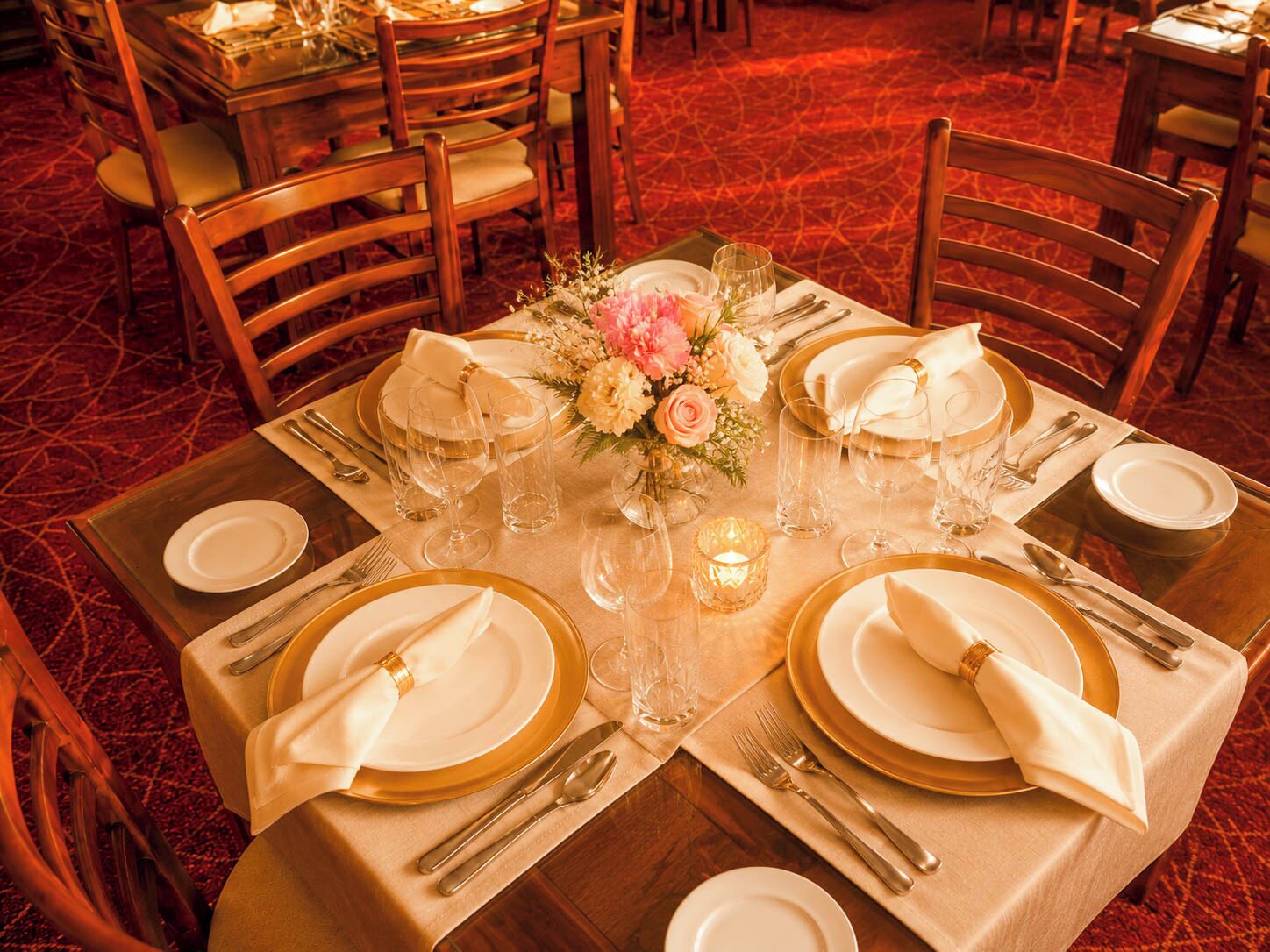Mesa de comedor dispuesta para seis personas, con platos con borde dorado, servilletas blancas y cubiertos.