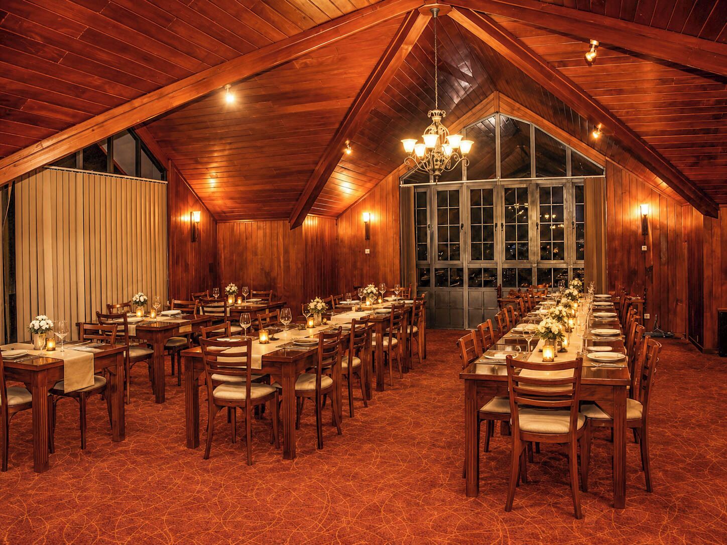 A large, well-lit dining hall with high ceilings and wooden paneling, featuring multiple tables set for dining.