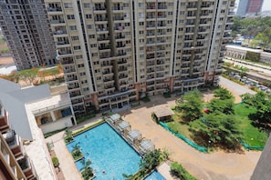 A high-rise building with multiple balconies, a swimming pool, and a landscaped area with trees and a small garden. - Velour by Redolive 2bhk 5 min Itpl Whitefield (Bengaluru)