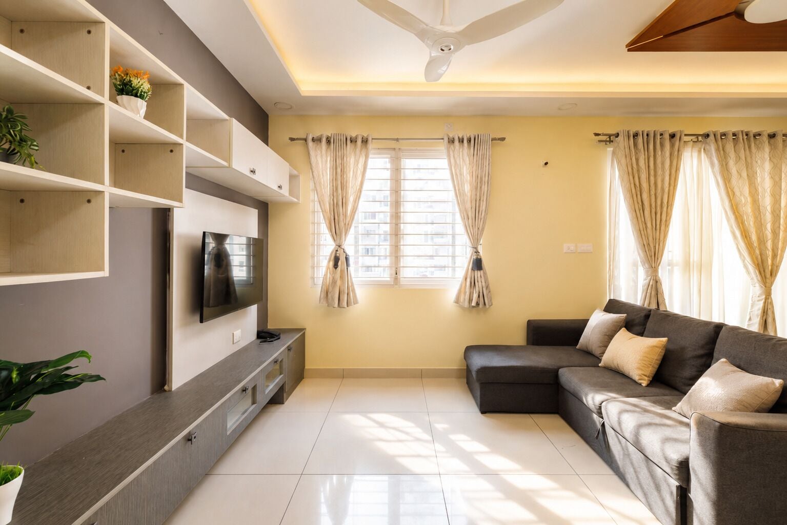 A modern living room with a flat-screen TV, a sofa, and a ceiling fan.