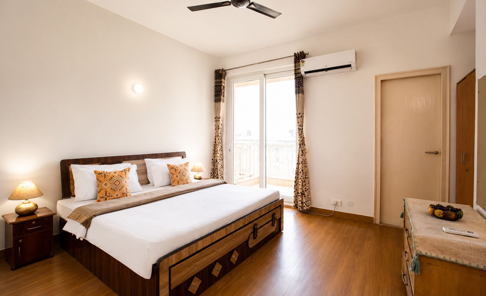 A bedroom with a bed, bedside tables, an air conditioning unit, a ceiling fan, and a view of the outside.