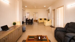 A modern living room with a sofa, a coffee table, a dining area, and a kitchen area. - Aravalli by Red Olive4bhk10min Apollocybercity (Gurugram)
