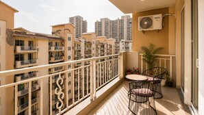 A balcony with a white railing, a table with chairs, a potted plant, and a window with an air conditioning unit. - Aravalli by Red Olive4bhk10min Apollocybercity (Gurugram)