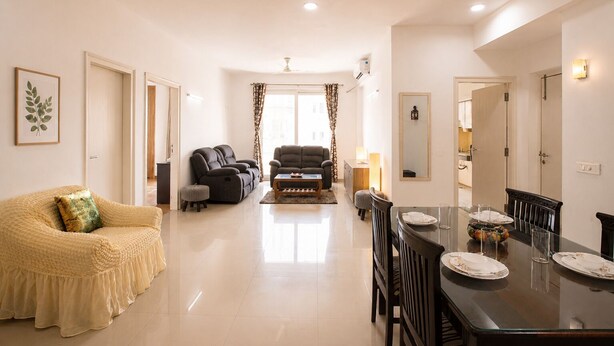 A modern living room with a sofa, two recliners, a dining table with chairs, and a kitchen area in the background. - Aravalli by Red Olive4bhk10min Apollocybercity (Gurugram)